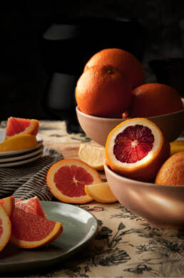 Blood oranges and cara cara oranges in bowls with dappled light