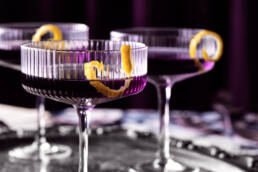 Three creme de violette cocktails with lemon garnish